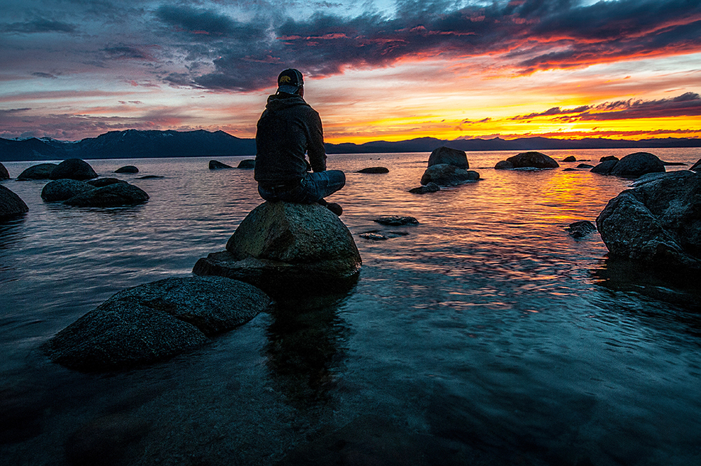 Man sitting alone on a rock in the middle of the water