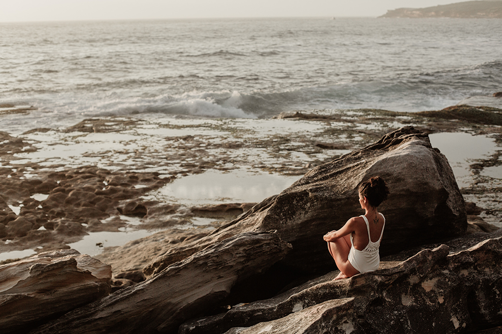 Woman sitting alone on a rock looking at the surf